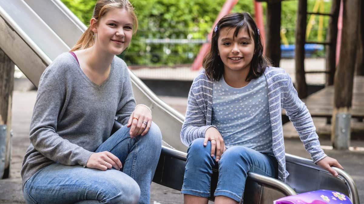 Malteser Schulbegleiterin sitzt mit Schülerin auf einer Rutsche.