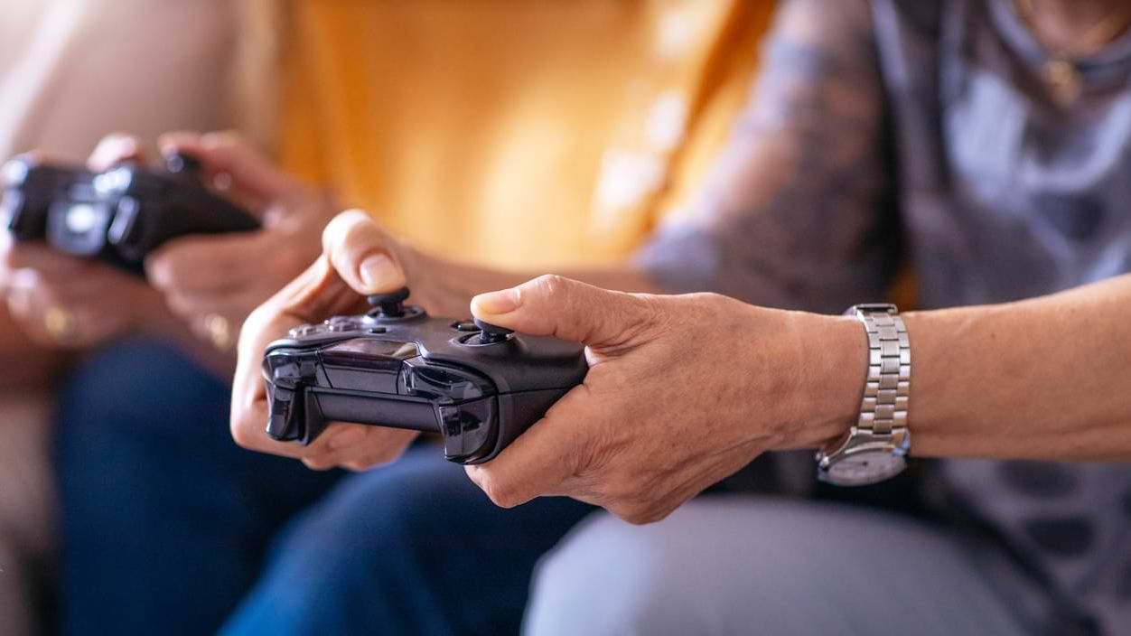 Eine ältere Person hält ein Gamepad mit beiden Händen.