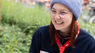 Junge Frau in Malteser Kleidung mit einer grauen Mütze sitzt im Freien an einer Schreibmaschine