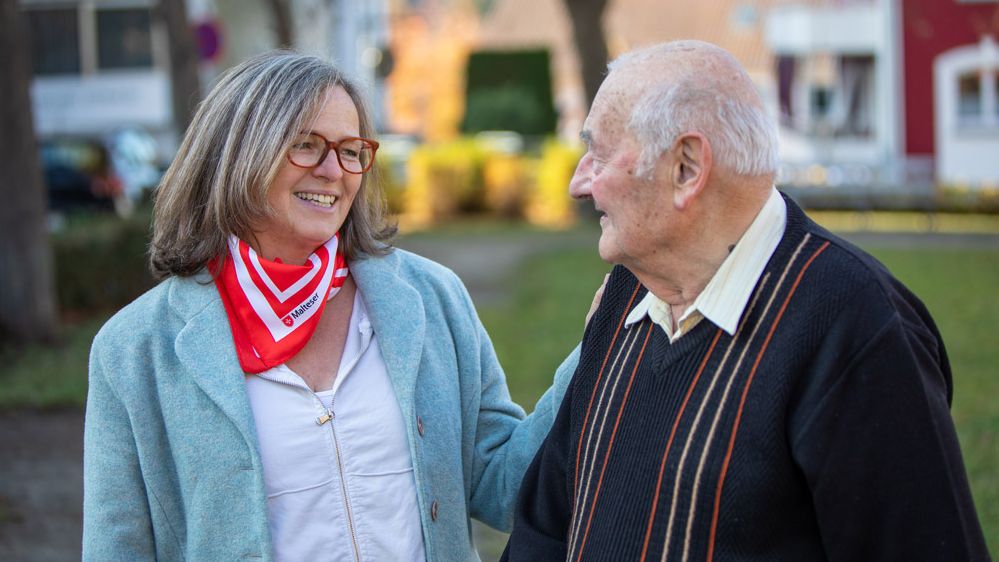 Eine Demenzbegleiterin und ein älterer Herr lachen gemeinsam im Freien.