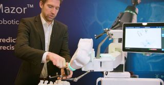 Person demonstriert den Wirbelsäulenroboter Mazor X mit Instrument und Modellwirbel-säule.