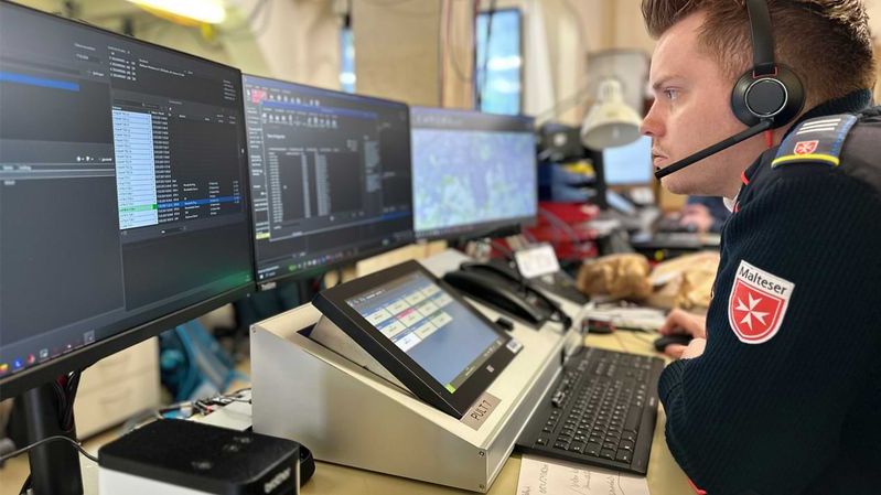 Ein Mann mit Headset in einer modernen Funkzentrale mit vielen Bildschirmen. 