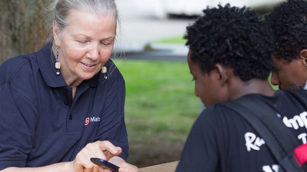 Ältere Frau zeigt jungen Flüchtlingen etwas auf dem Smartphone.