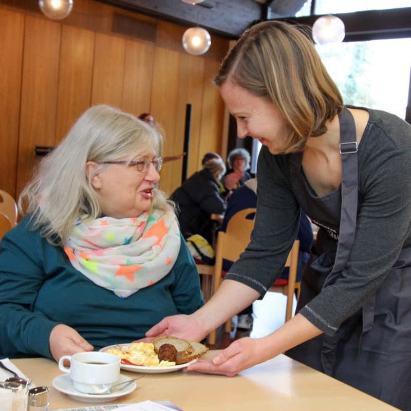 Eine Frau des Malteser Wohlfühlmorgenprogramms serviert das Essen.