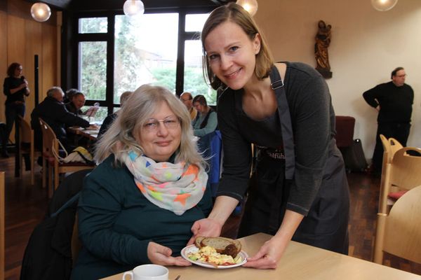 Beim Malteser Wohlfühlmorgen reicht eine Frau einer anderen Frau am Tisch einen gefüllten Teller. 