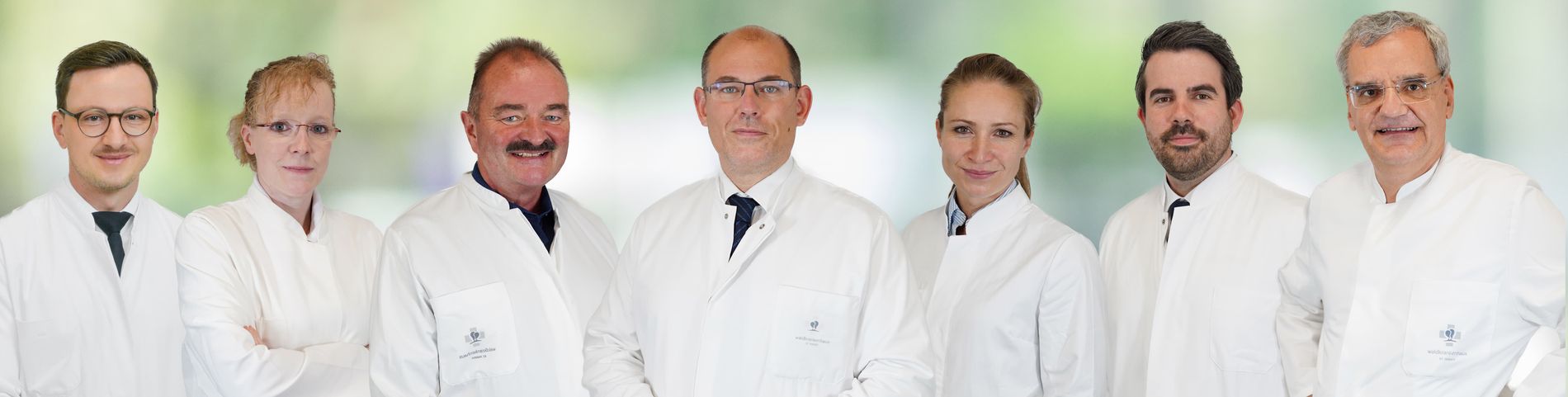 Sieben medizinische Fachkräfte der Klinik für Orthopädie und Unfallchirurgie in weißen Kitteln stehen nebeneinander.