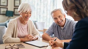 Zwei lächelnde ältere Menschen in einem Beratungsgespräch mit einer Frau.