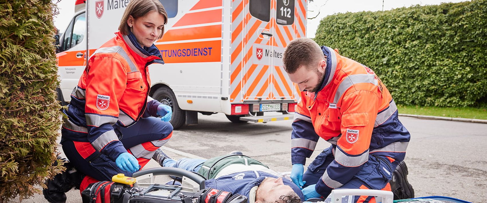 Eine Rettungssanitäterin und ein Rettungssanitäter versorgen einen Verletzten, der auf der Straße liegt. 