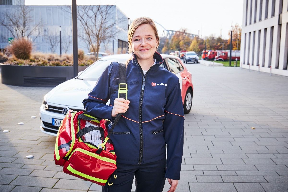 Junge Frau vor einem Kleinwagen mit Aufdruck der Malteser.