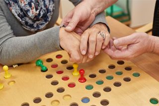 Zwei Hände unterstützen Hände von jemand anderem beim Mensch ärger dich nicht spielen