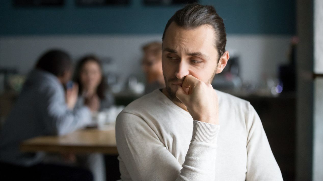 Ein junger Mann sitzt allein abseits von einer Menschengruppe