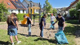 5 Personen der Malteser Jugend, die auf einem Spielplatz mit Müllzangen Müll aufsammeln.