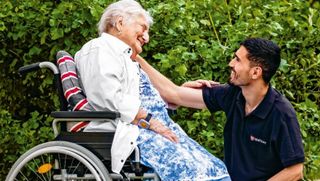 Ein Malteser Pfleger lacht herzlich mit einer älteren Frau im Rollstuhl.