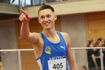 Ein Leichtathlet im blauen Trikot mit Startnummer 405 zeigt auf etwas außerhalb des Bildes.