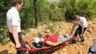 Zwei Sanitäter tragen eine Verletzte auf einer Trage den Berg runter.
