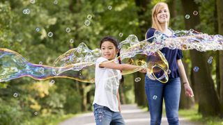 Junge macht große Seifenblasen und wird von Malteser Helferin begleitet.