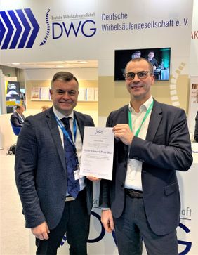 Zwei Männer im Anzug halten gemeinsam eine Urkunde mit der Aufschrift „Georg-Schwedt-Preis 2023“ in die Kamera.