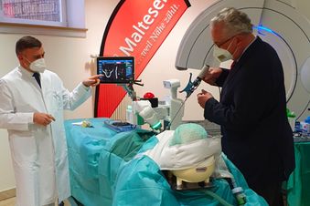 Arzt demonstriert einem Besucher an einem Modellkopf den Einsatz eines OP-Roboters mit Monitoranzeige.