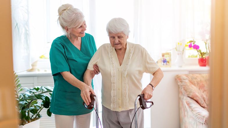 Pflegekraft stützt ältere Frau mit Rollator.