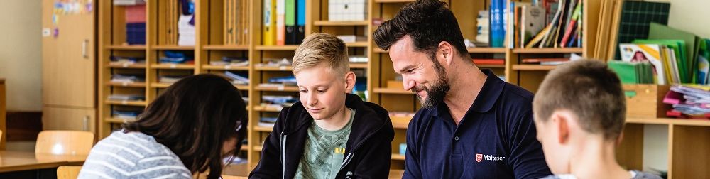 Ein Schulbegleiter mit drei Kindern an einem Schultisch