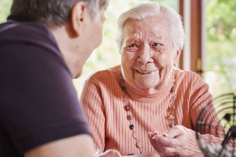 Eine ältere Frau spricht mit einer anderen Frau, beide sitzen an einem Tisch.