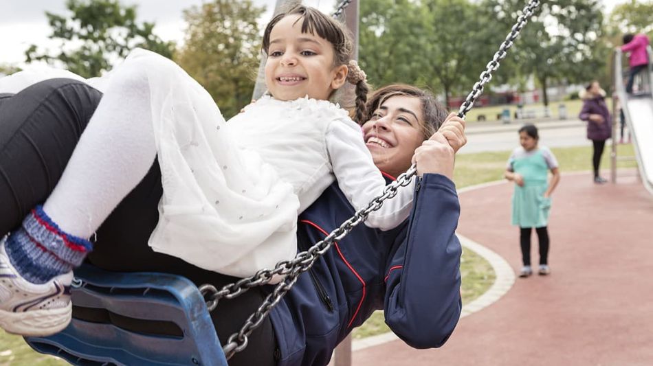 Es wird eine junge Frau gezeigt, welche mit einem Kind schaukelt.