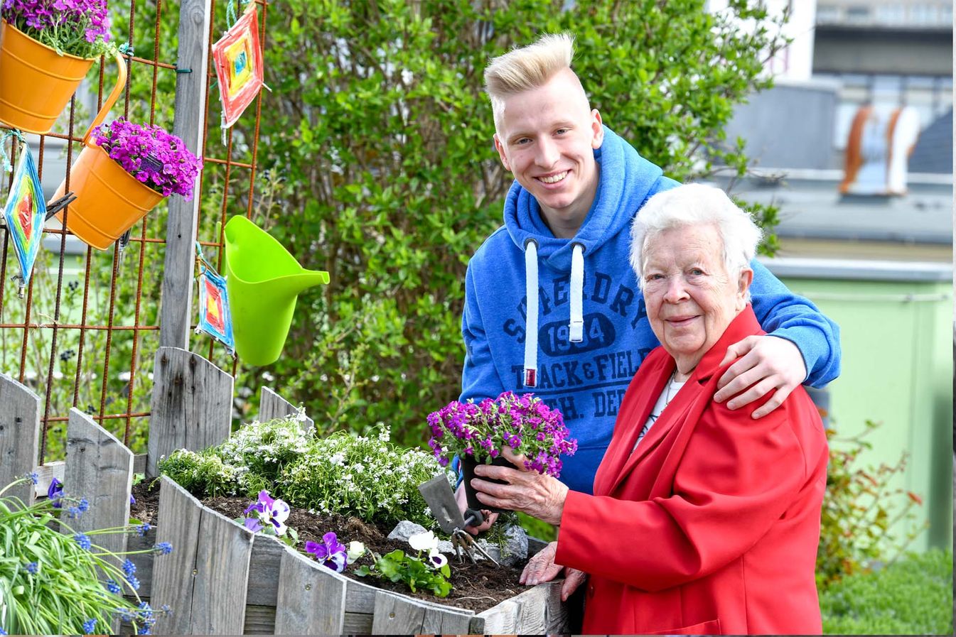 Begleiter des sozialen Dienstes pflanzt mit Bewohnerin Blumen ein