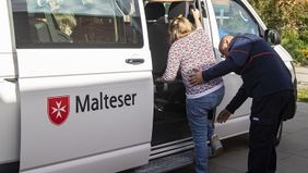 Ein Mann hilft einer Person beim Einsteigen in einen Kleinbus.