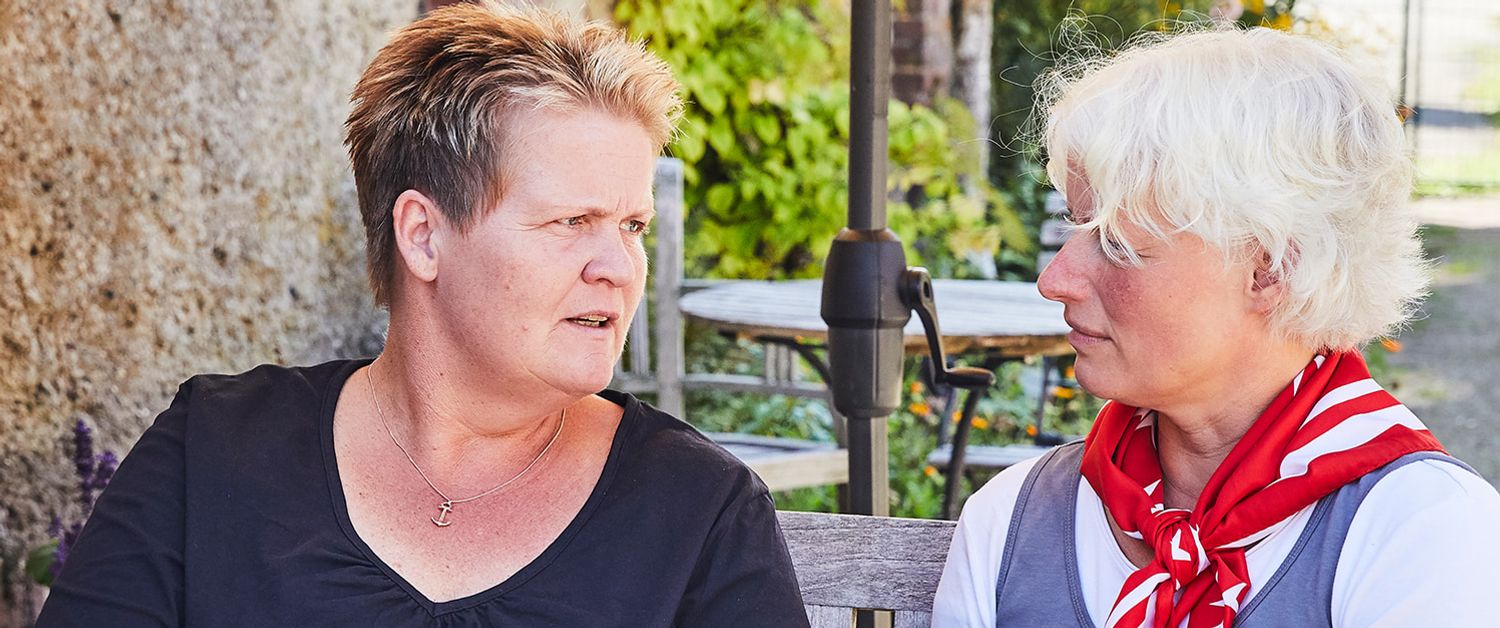 Zwei Frauen sitzen im Garten im Tisch und führen ein Gespräch.