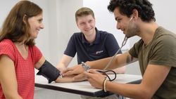 Junger Mann misst bei junger Frau den Blutdruck am Arm.