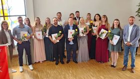 Junge Männer und Frauen halten Zeugnisse und Blumen in der Hand.