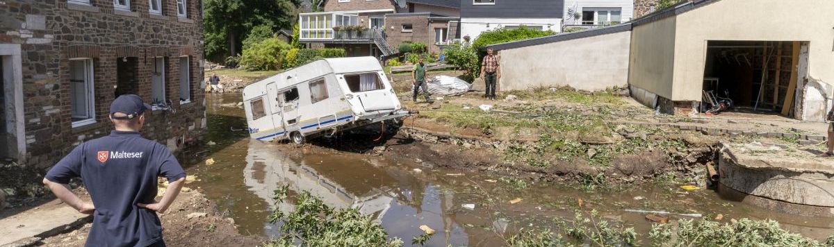 Ein Junger Mann mit in die Hüften gestemmten Armen schaut auf eine von Hochwasser zerstörter Straße.