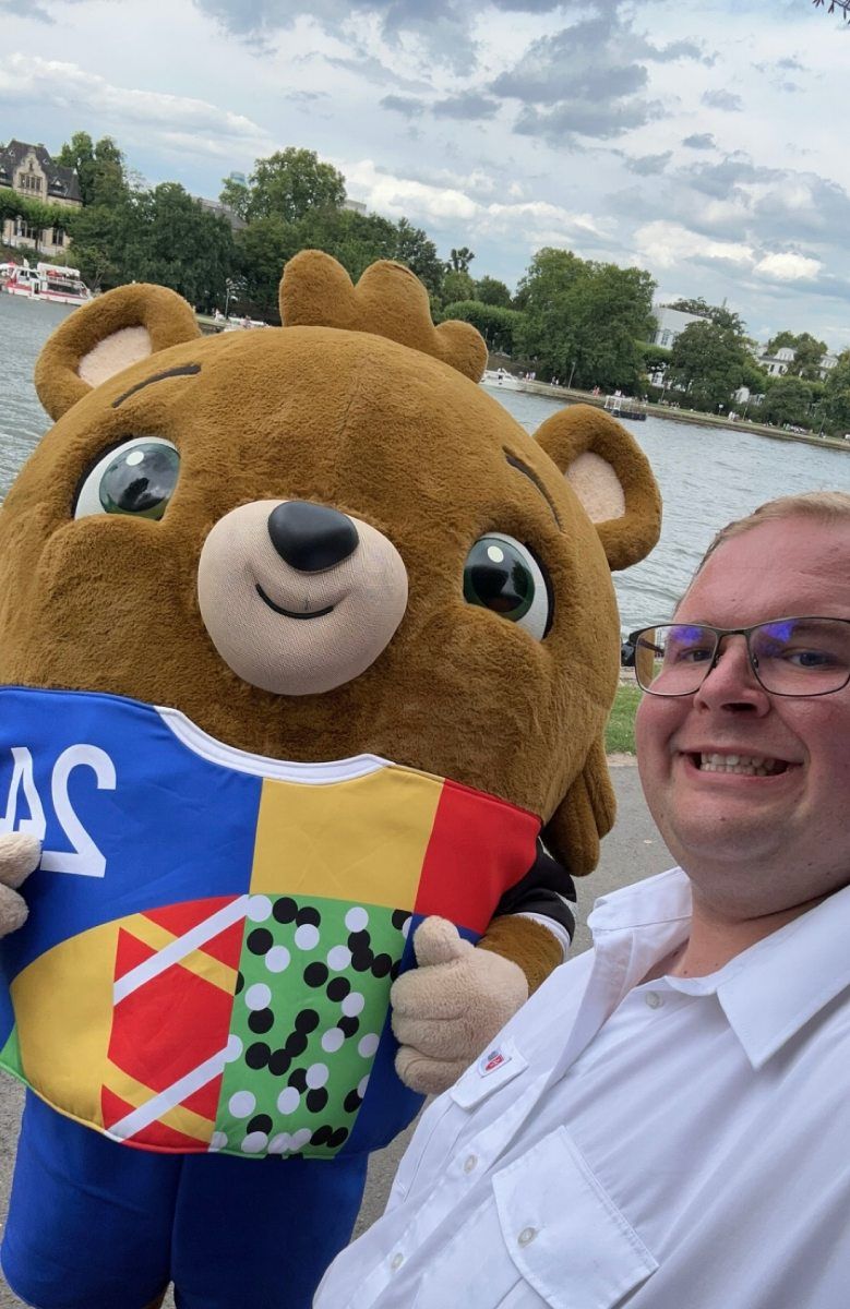 Ein lächelnder Mann mit Brille mit dem Masskottchen der Fußball-EM 2024