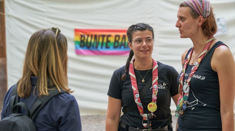 Drei Frauen in dunklen T-Shits stehen sich gegenüber und unterhalten sich miteinander. Zwei der Frauen tragen Halstücher. 