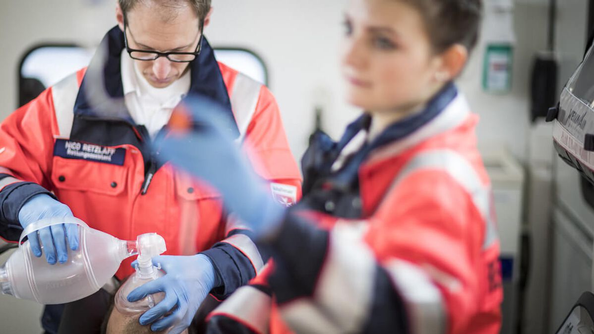 Zwei Notfallsanitäter legen einem Patienten im Krankenwagen eine Beatmungsmaske auf