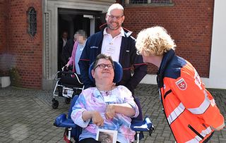 Frau im Rollstuhl und zwei Malteser Helfende vor Basilika