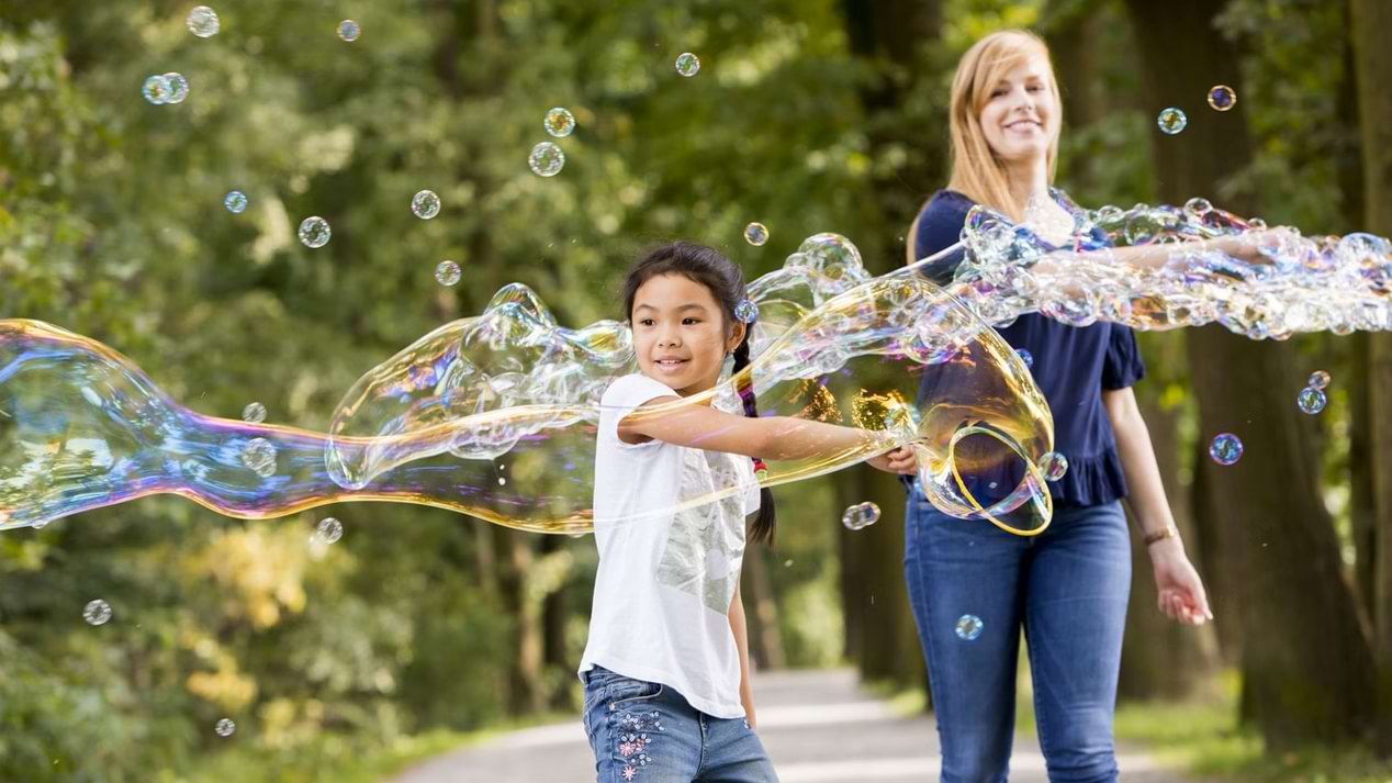 Eine junge, lächelnde Frau und ein Mädchen machen Seifenblasen.