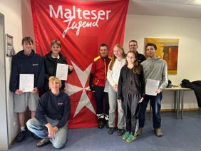 Acht Jugendliche stehen vor einem Malteser Jugend Banner und lächeln in die Kamera.
