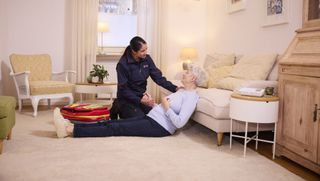 Hand einer älteren Frau mit einem Wasserglas, am Handgelenk ein roter Hausnotrufknopf