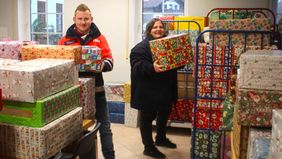 Zwei Menschen stapeln viele Pakete mit weihnachtlicher Verpackung.