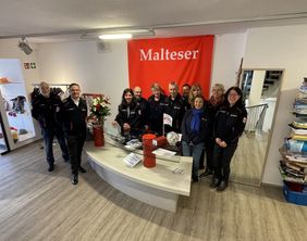 Die ehrenamtlichen Helferinnen und Helfer der Malteser Werdohl auf einem Gruppenfoto hinter dem Verkaufstresen des Kleiderlädchens.