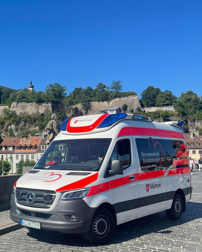 Ein Krankenwagen, der von den Maltesern für das Projekt Herzenswunschkrankenwagen eingesetzt wird vor schöner, städtischer Kulisse