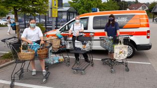 Drei Personen stehen mit gefüllten Einkaufswägen vor dem Malteser-Fahrzeug.