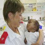A care worker holds an infant in her arms.