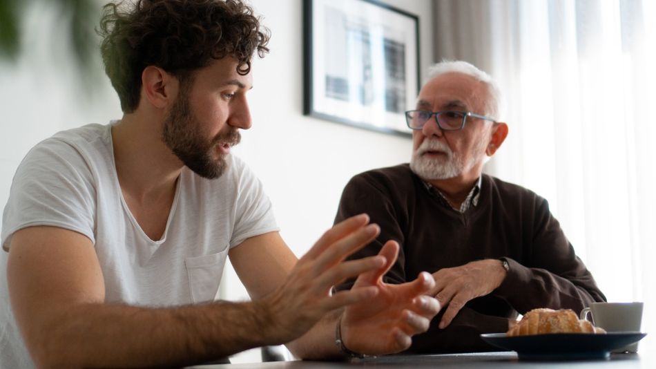 Ein junger Mann mit einem älteren Mann an einem Tisch im Gespräch. 