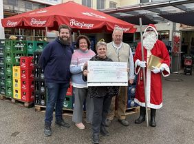 Vier Personen mit Nikolaus stehen vor einem Getränkemarkt und hält einen Spendenscheck hoch.