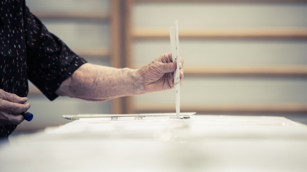 Es wird ein Stimmzettel gezeigt, welcher in eine Wahlurne geworfen wird.