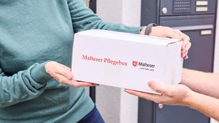 Nahaufnahme eines Pakets mit der Aufschrift "Malteser Pflegebox" bei der Lieferung an der Haustür.