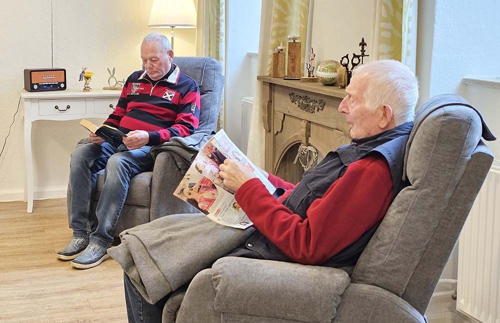 Zwei Männer sitzen am Kamin in gemütlichen Sesseln und lesen.