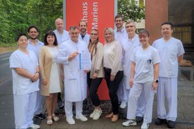 Eine Gruppe von Personen steht vor einem Gebäudeeingang, einer hält ein Zertifikat in seinen Händen.